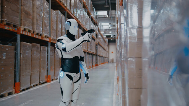 Intelligent humanoid robot pointing scanner at barcode while standing in warehouse aisle. Processing product information or tracking inventory updates during automated supply chain operation.