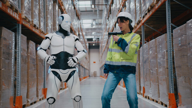 Woman holding barcode scanner while robot poses with arms wide in funny moment at distribution center.