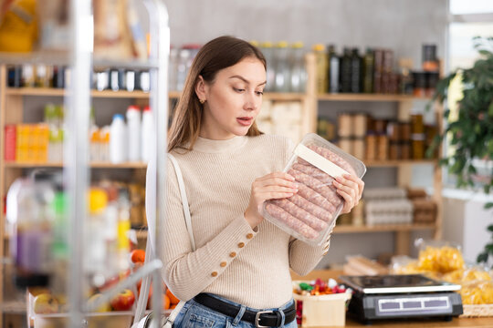 Girl looking at raw bbg sausage in store. Market visitor choose consider raw meat semi-finished goods. Buyer pick up meat for cooking dinner