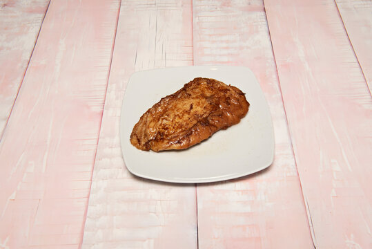 Golden triangular torrija soaked in caramelized syrup rests on a white rectangular plate over a whitewashed pink wooden surface.