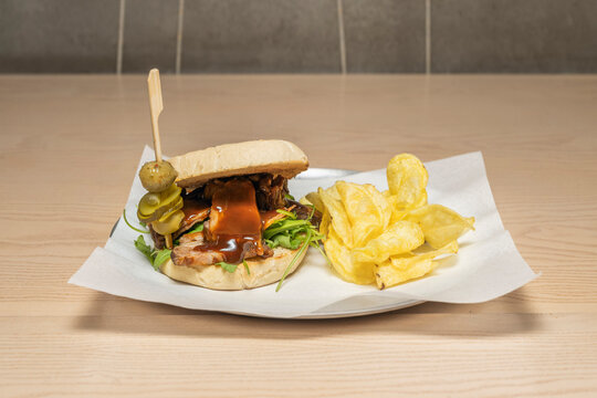A delicious sandwich in a bread roll filled with BBQ rib meat, fries and a skewer.