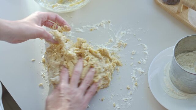 Woman kneads dough by hand on floured kitchen counter beside metal sifter