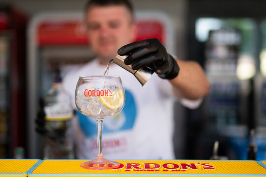 LVIV, UKRAINE - JUNE 21, 2024: Professional bartender in black gloves pouring gin into a branded Gordon's glass with ice and lemon