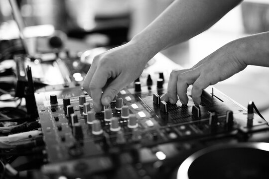 Black and white close-up of DJ hands mixing music on professional equipment