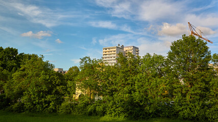 Modern residential high-rise apartment building and a construction tower crane rising above a lush green forest wall of trees under a blue sky. © beautiful-photo.de