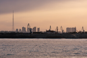 Obraz premium Industrial waterfront with cranes and city skyline during colorful sunset. Blagoveshchensk, Russia