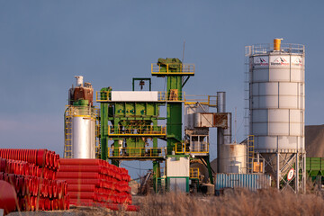 Obraz premium An asphalt plant with silos, machinery, and construction materials under clear sky in industrial setting