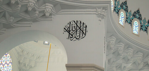 Close up of circular Arabic calligraphy mural on white wall with muqarnas details in traditional architecture © catocala