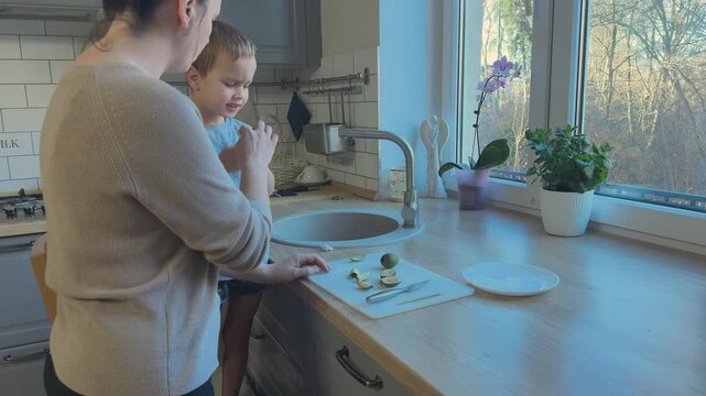Child tastes fruit again while mother smiles nearby. Warm parenting moment and emotional family connection.