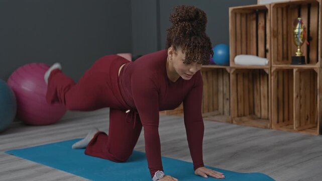 Woman performing bird dog exercise with extended arm and leg on blue yoga mat in studio; serenity balance.