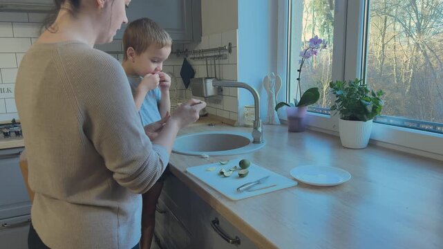 Child tastes feijoa fruit and reacts with funny face showing dislike. Real emotion moment in family kitchen.
