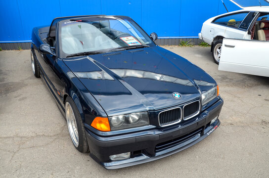 Black BMW E36 convertible at an outdoor car show. Features a lowered stance, custom deep-dish rims, and M style bumper