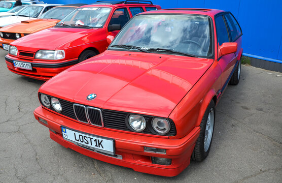 Red BMW E30 3 Series coupe with a sunroof and aftermarket wheels sits in a row of classic cars