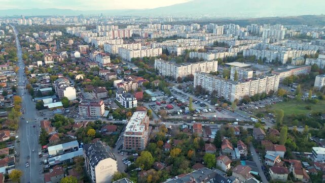 Drone aerial panorama of a densely populated residential district in Sofia, Bulgaria featuring apartment buildings, city streets, parks, and the skyline with Vitosha Mountain in the background. Wide e