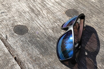 Reflecting sunglasses on sunny spring day in nature. Wooden background. © Martin of Sweden