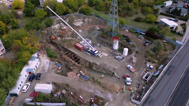 Vertical aerial drone footage of an active construction site where a drilling rig and construction crew perform foundation and ground engineering work. The scene highlights excavation, heavy machinery