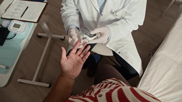POV shot of unrecognizable patient with diabetes sitting in front of doctor performing finger glucose test using glucometer during diabetic health examination in medical office