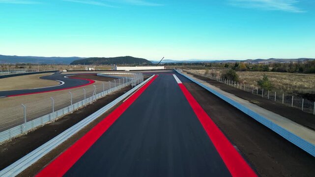 Aerial view of a modern motorsport racetrack with sweeping curves, pit buildings, and wide runoff areas set in an open rural landscape near a town and distant hills