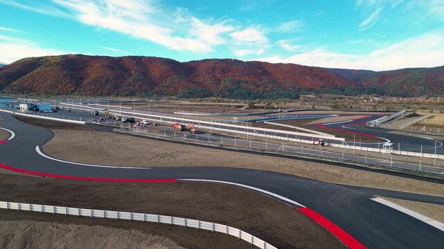 Aerial view of a modern motorsport racetrack with sweeping curves, pit buildings, and wide runoff areas set in an open rural landscape near a town and distant hills