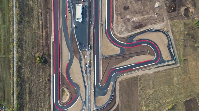 Aerial view of a modern motorsport racetrack with sweeping curves, pit buildings, and wide runoff areas set in an open rural landscape near a town and distant hills