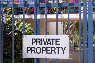 "PRIVATE PROPERTY" warning sign on a metal security fence  blurred residential building in the background. Security and boundary of older apartment or units in a suburban neighborhood of Australia © Doublelee