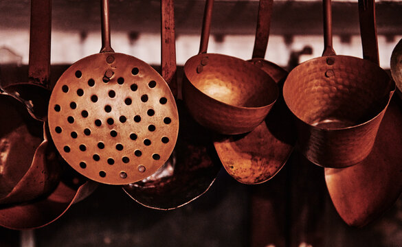 collection of traditional hammered copper kitchen utensils hanging up, including ladles, a skimmer, and small pots