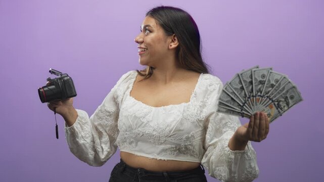 Woman photographer holds dslr camera in one hand and fans us dollar bills with the other in a purple studio, smiling and posing; creator monetization confidence.