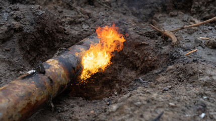 Fototapeta premium Dangerously cracked pipe with bright flames and smoke in a trench, buried in a deep ditch of brown soil, illustrating a hazardous leak