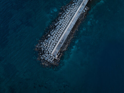 Aerial view of the concrete block breakwater protecting the coast of the Island of Ortigia surrounded by deep blue sea water in Syracuse, Sicily, Italy.