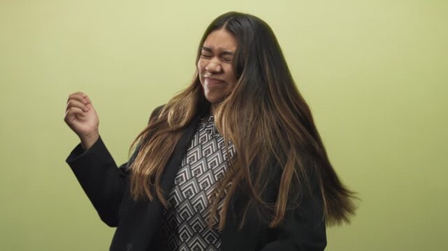 Woman with hand mid gesture, eyes closed, hair flipping across face, wearing blazer and patterned shirt in studio; playful confidence.