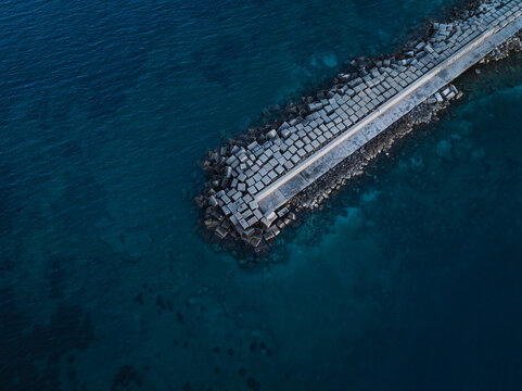 Aerial view of the concrete block breakwater protecting the Island of Ortigia coastline surrounded by deep blue Mediterranean waters in Syracuse, Sicily, Italy.