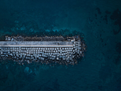 Aerial view of a concrete breakwater and protective stone blocks surrounded by deep blue sea water at the Island of Ortigia Syracuse, Sicily, Italy.