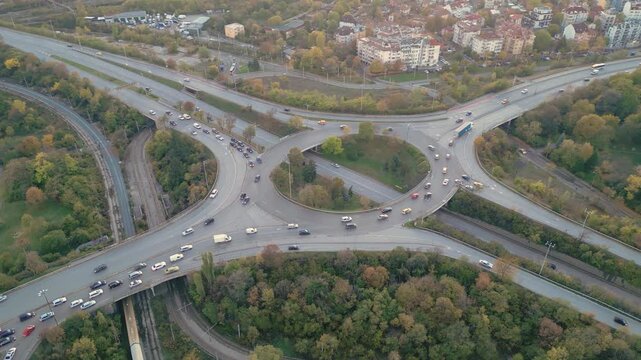 Aerial drone footage of a large highway interchange featuring a circular flyover, multiple connecting roads, and steady vehicle traffic during daylight. The clip showcases modern transportation infras