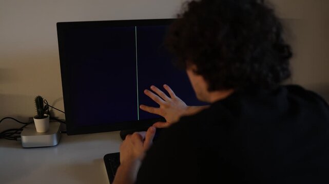 Young curly haired man feeling stressed after computer monitor failure black screen with vertical glitch stripe home office technology problem cinematic indoor atmosphere realistic frustrated reaction