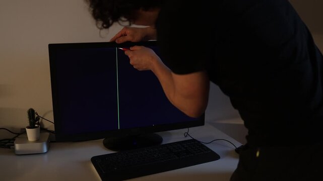 Young man attempting to fix malfunctioning computer monitor in apartment modern digital lifestyle technical repair and home office problem cinematic scene