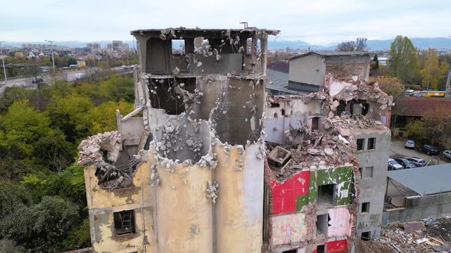 Aerial drone footage of a partially demolished industrial building featuring large concrete silos, collapsed masonry walls, and piles of construction debris. The scene documents urban redevelopment, i