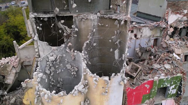 Aerial drone footage of a partially demolished industrial building featuring large concrete silos, collapsed masonry walls, and piles of construction debris. The scene documents urban redevelopment, i