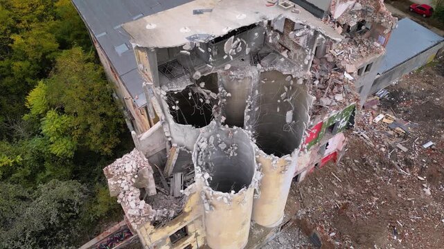 Aerial drone footage of a partially demolished industrial building featuring large concrete silos, collapsed masonry walls, and piles of construction debris. The scene documents urban redevelopment, i