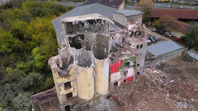 Aerial drone footage of a partially demolished industrial building featuring large concrete silos, collapsed masonry walls, and piles of construction debris. The scene documents urban redevelopment, i