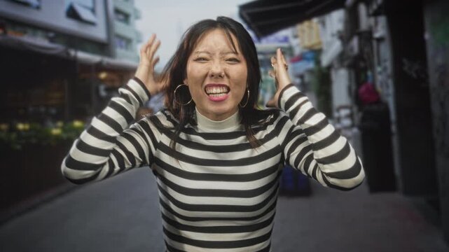 Woman in black and white striped sweater clutching her collar and clenching fists while shouting on a narrow street market lane, head tilted back in motion; joy celebration.