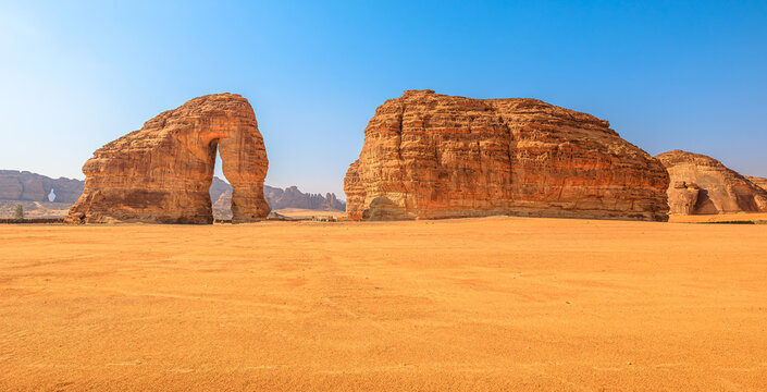 Elephant Rock (Jabal AlFil) rises from the vast orange sands of AlUla, Saudi Arabia, a majestic sandstone formation under a clear blue sky in a remote desert landscape panorama 16:9