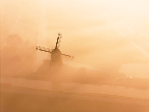 Aerial view of the historic windmill at Polder de Lage Hoek shrouded in thick morning mist during a golden sunrise Hoogwoud, Noord-Holland, Netherlands.