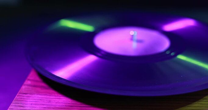 Modern turntable with vinyl record on table in color lights, closeup. Camera moving left