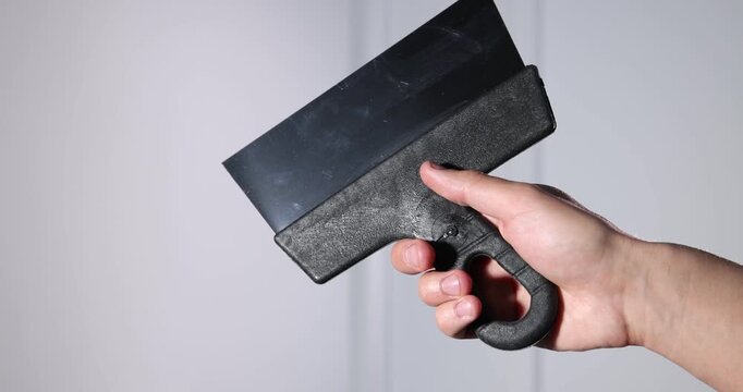Handyman with putty knife on light background, closeup