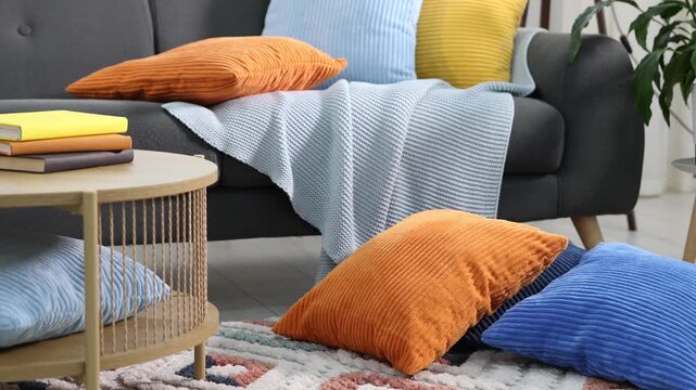 Soft cushions in colorful pillowcases on sofa and table with books indoors. Camera moving down