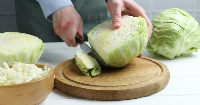 Woman cutting fresh cabbage at white wooden table, closeup