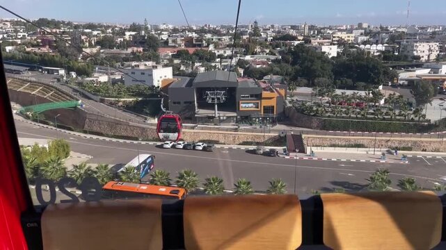 POV cable car ride descending toward modern Agadir station with panoramic urban cityscape and transportation infrastructure in Morocco