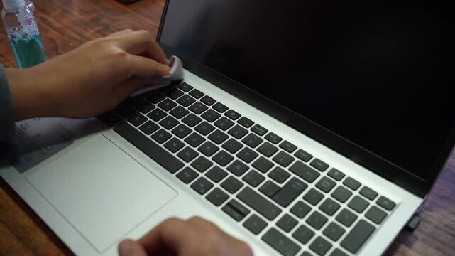 Person cleaning and disinfecting a laptop keyboard