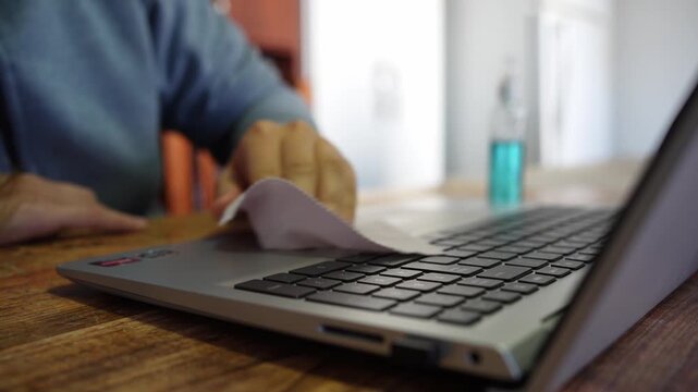Person sanitizing a laptop keyboard with spray