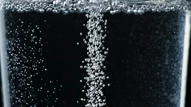 Close-up shot of refreshing clear carbonated water with rising bubbles, showcasing effervescence in a glass against a dark background, providing a crisp and invigorating visual